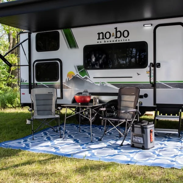 Campsite Accessories laid out with grill, camping chairs, table, patio mat and cooler