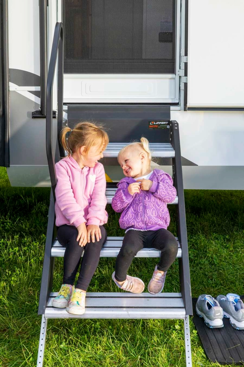 Young girls sitting on a Lippert Solid Step RV step with easy assist handrail