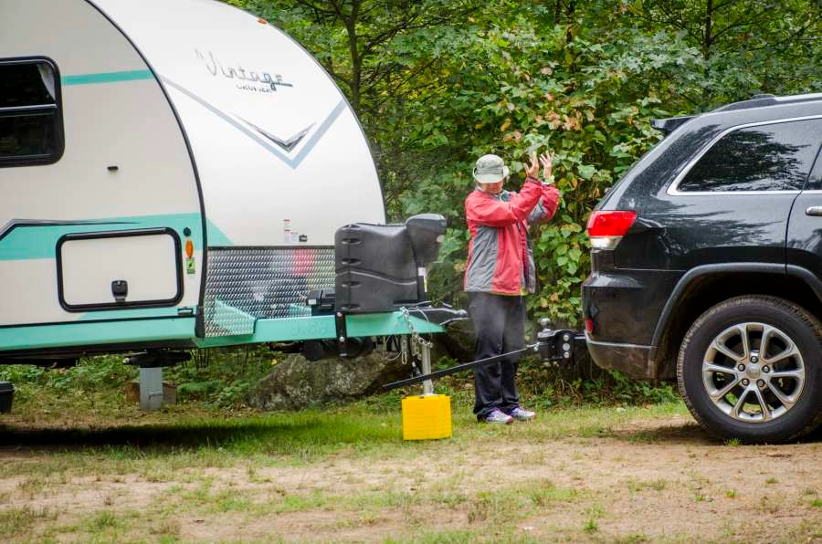 Person setting up weight distribution hitches for trailering, standing between their vehicle and camper
